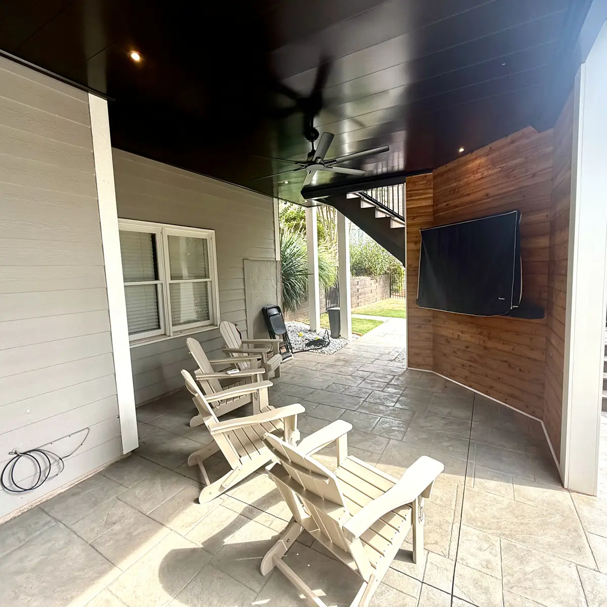 Under-deck covered patio with wood accent wall and outdoor TV