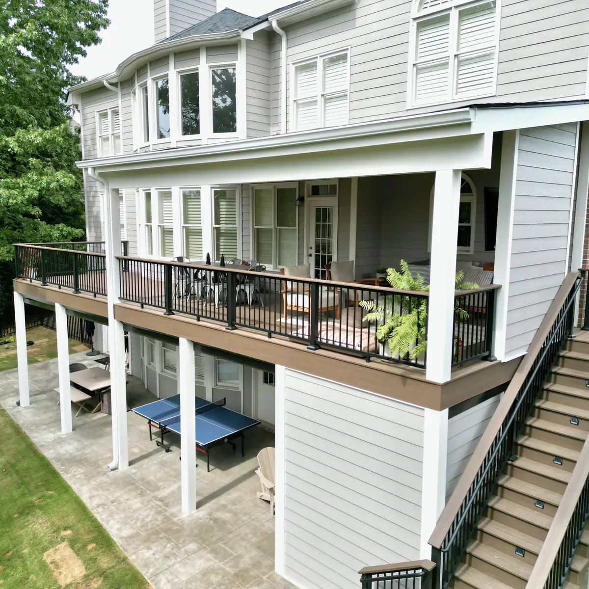 Elevated covered deck with white columns, black railings and stairs to the yard