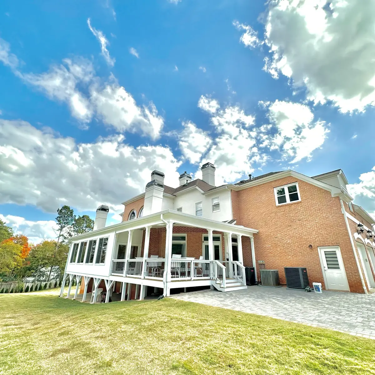 Wraparound covered porch addition on a brick home under blue sky