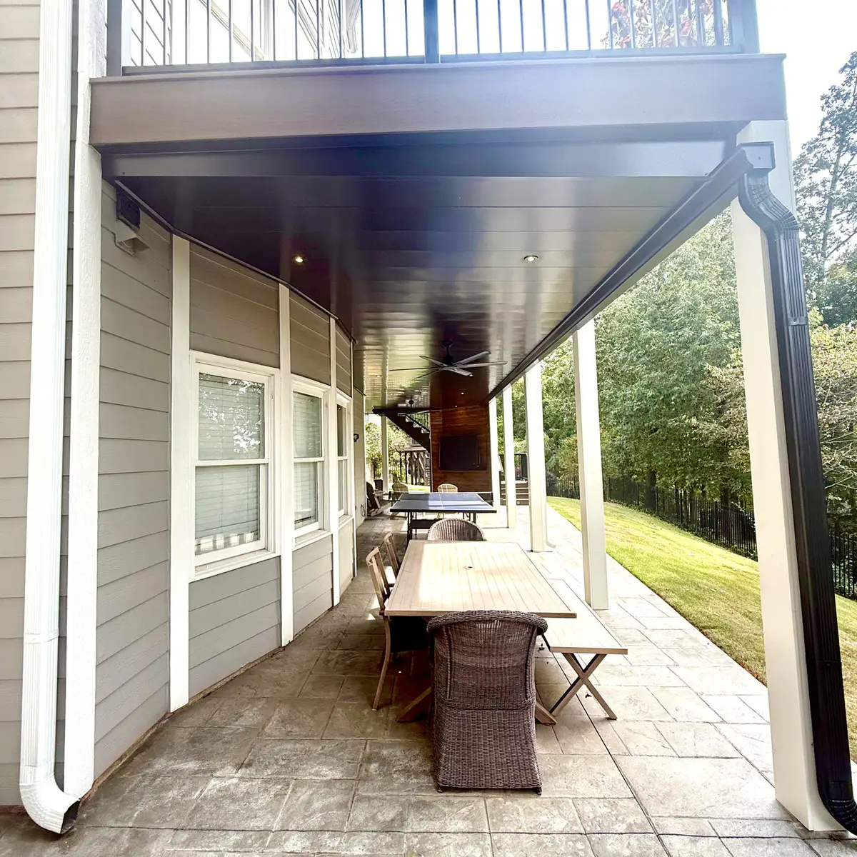 Covered patio under a deck with dark ceiling and dining table