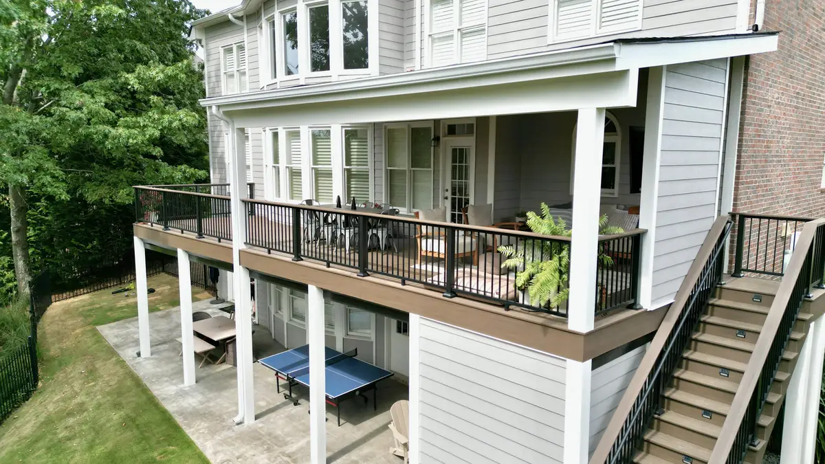 Long elevated covered deck with stairs on a grey-sided home backing to woods