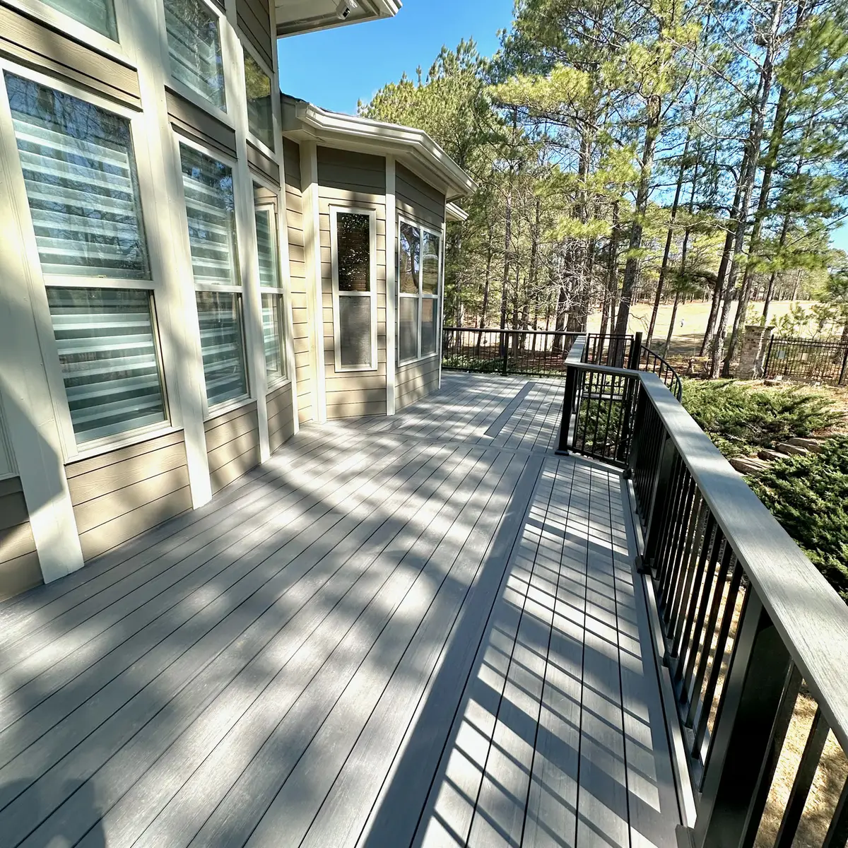 Long composite deck with black railings in a wooded lot