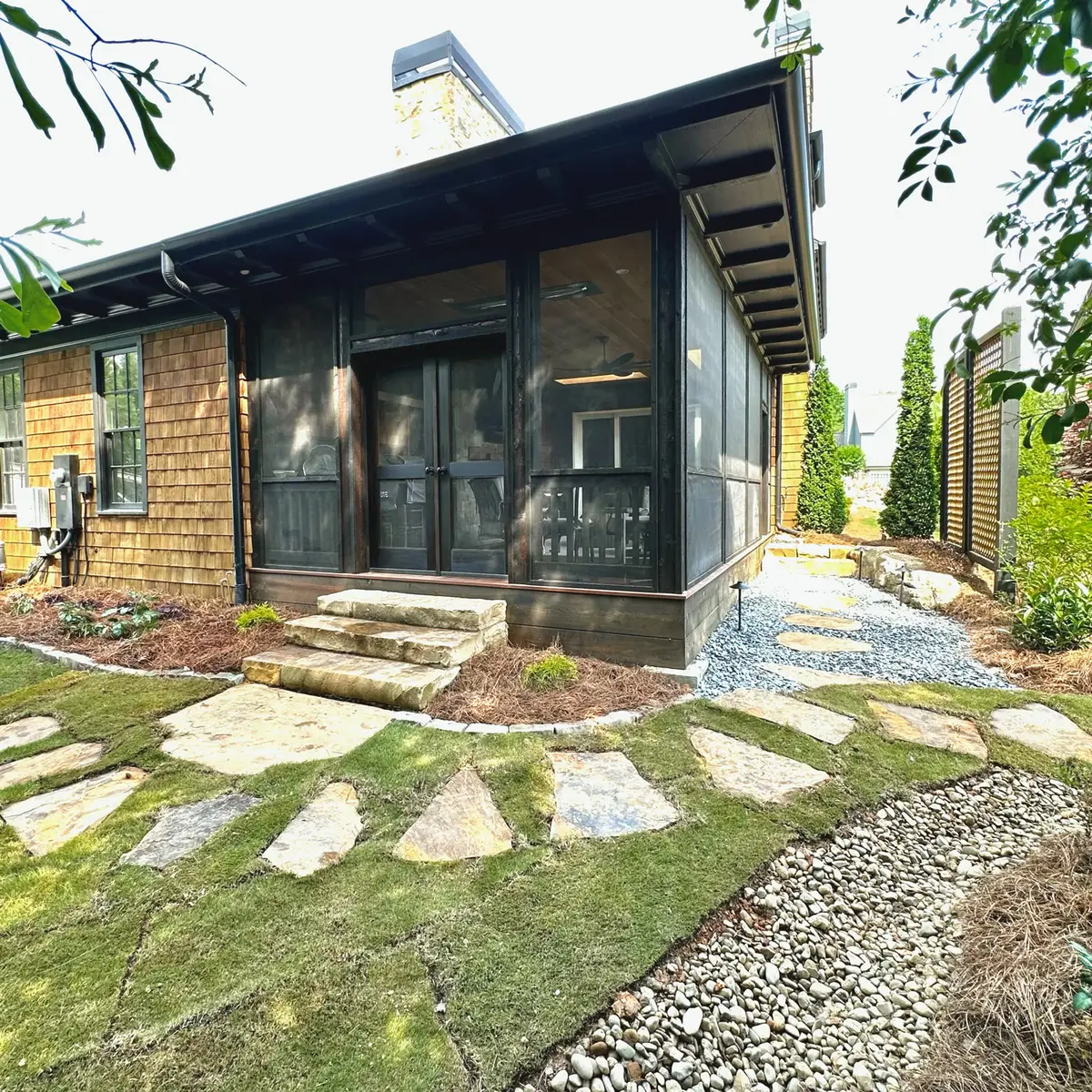 Dark-stained screened porch addition with flagstone path and gravel