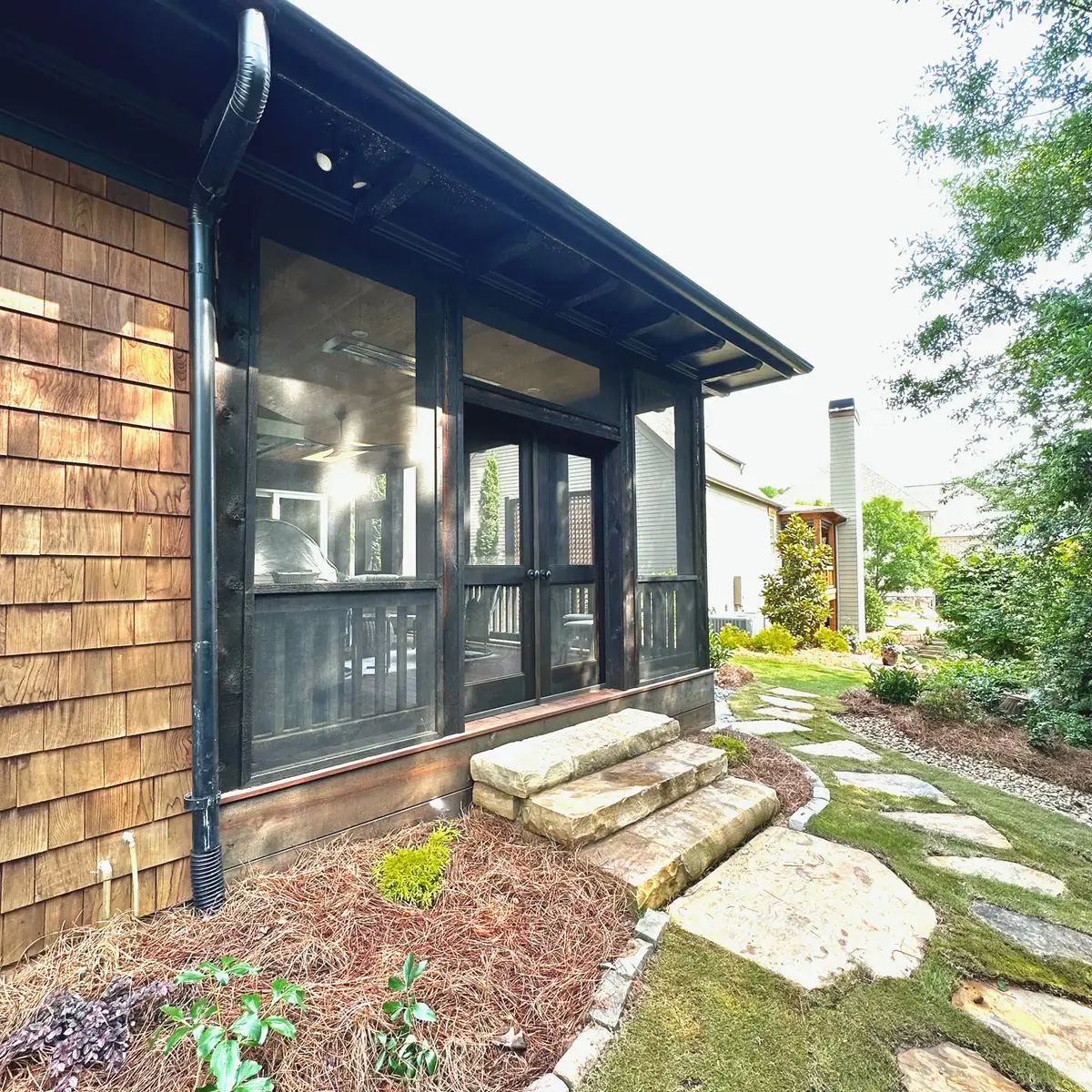 Exterior of a dark-framed screened porch with stone steps