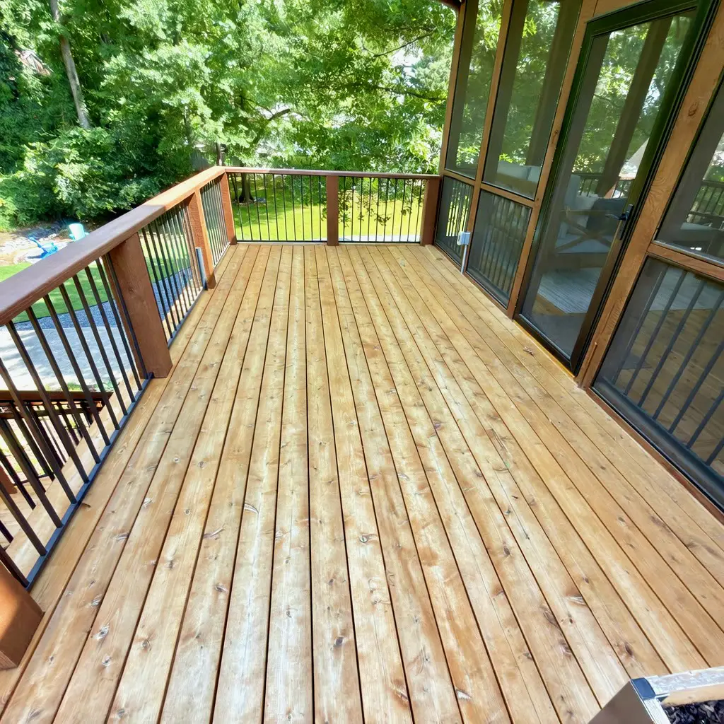 New pressure-treated wood deck with cedar-stained railing beside a screened porch