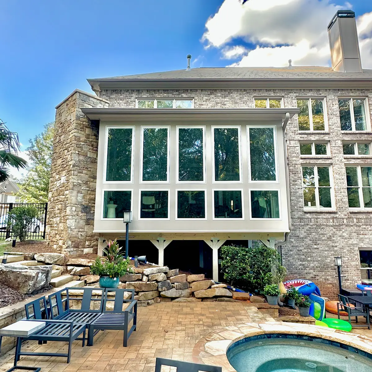 Sunroom addition with large windows above a stone patio and hot tub