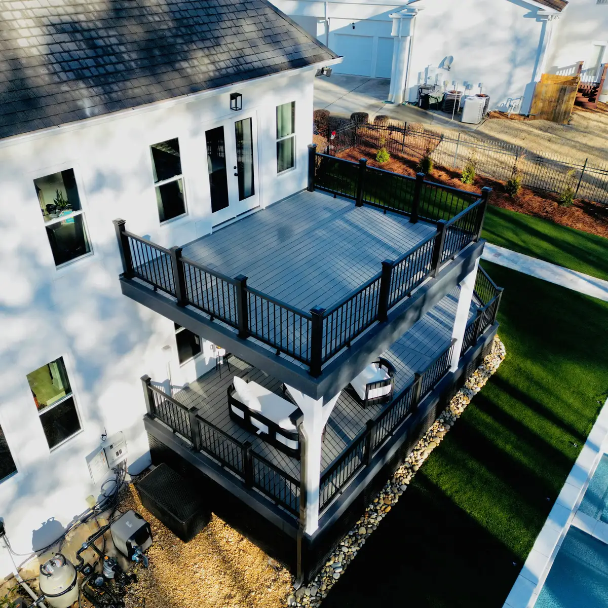 Aerial view of a stacked two-story deck with black railings beside a pool and turf