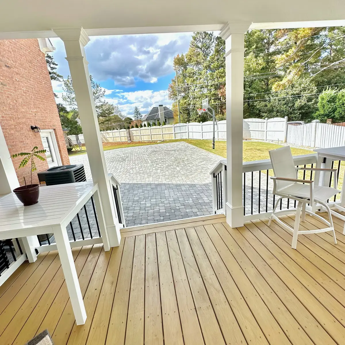 Covered deck with white posts and railings overlooking a paver driveway