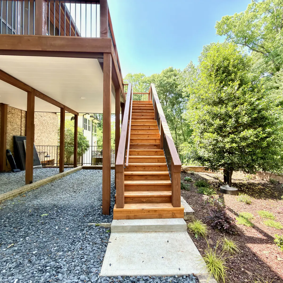 Stained wood deck stairs beside a gravel under-deck area