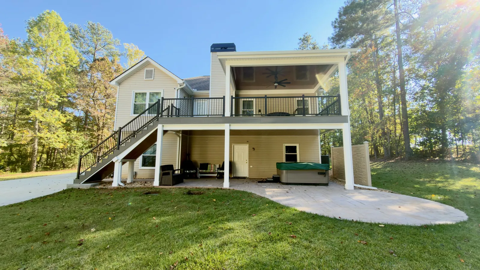 Douglas County covered deck from the yard: a shingled roof over composite decking and black rails, with seating and a hot tub in the dry space below