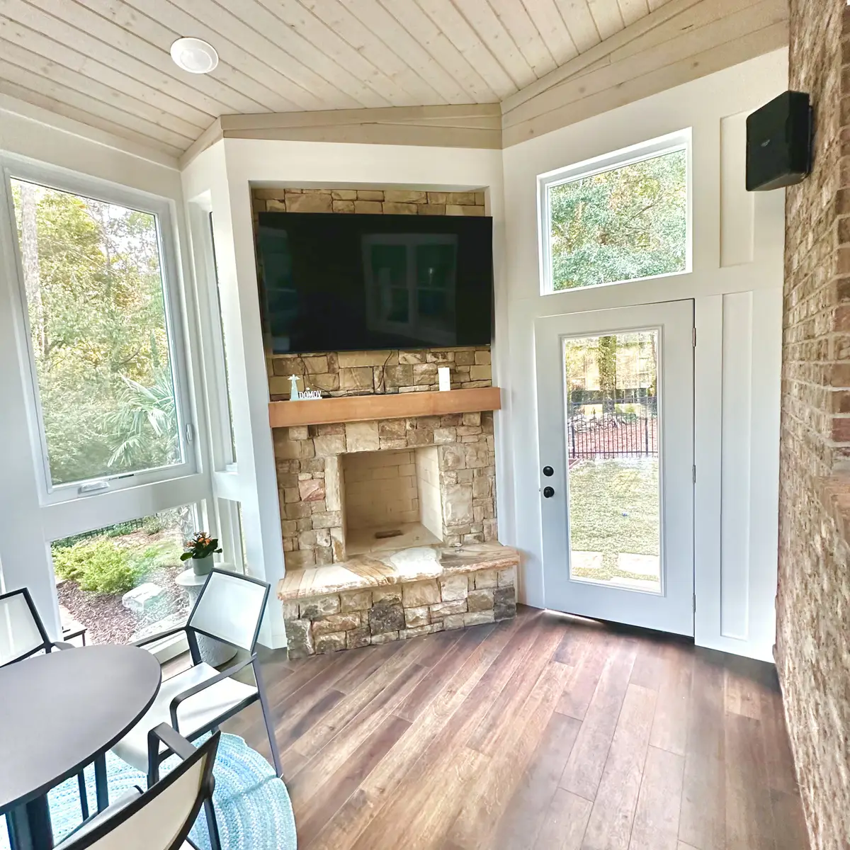 Sunroom with stone fireplace, mounted TV and wood-look flooring