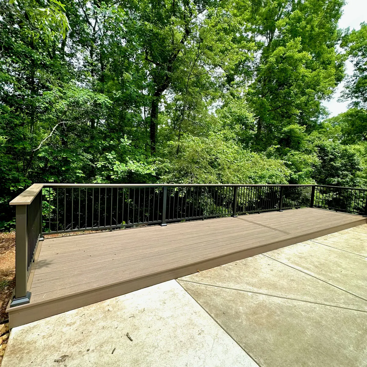 Composite deck with black aluminum railings beside a concrete pool deck
