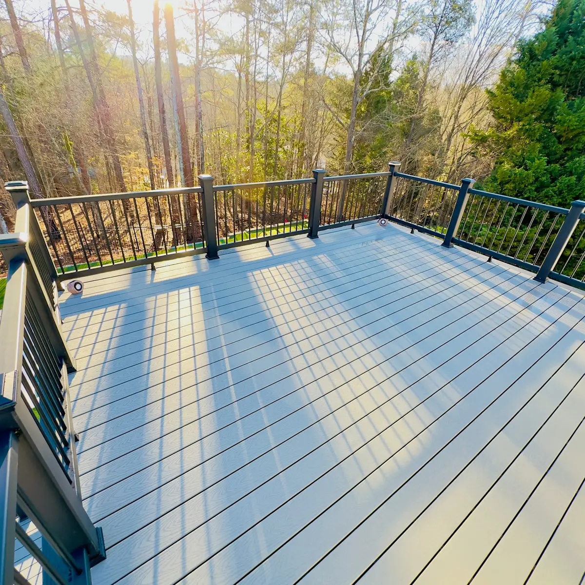 Grey composite deck with black railings facing woods